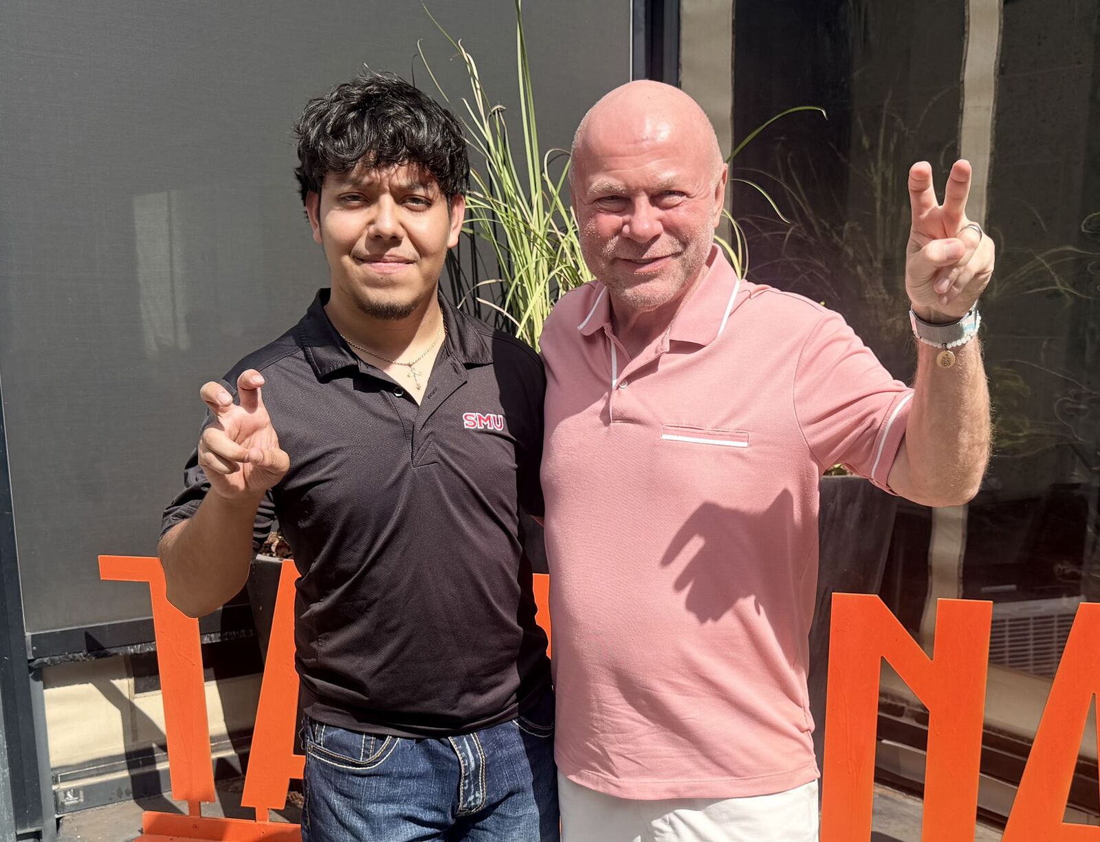 Miguel Gutierrez in an SMU polo and Bert Hibl in a pink polo, both giving the Pony Up hand sign outside Taverna