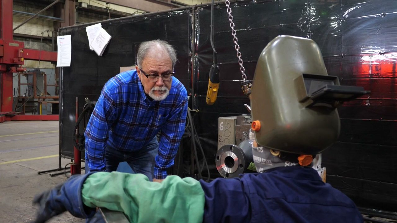 John Rogers leaning in to talk with a welder at a weld station